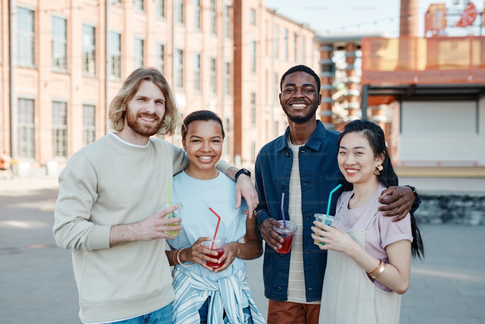 Waist up portrait of diverse group of people smiling at camera while enjoying Summer in city