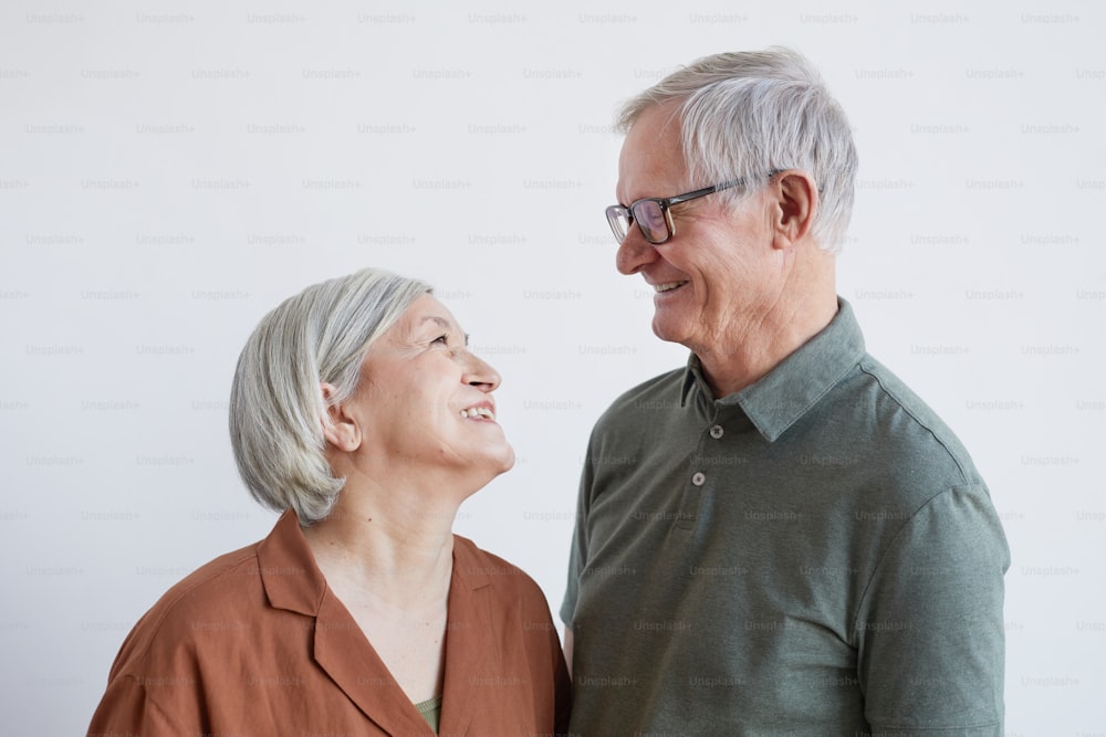 Ritratto di coppia anziana felice che si guarda l'un l'altro con amore mentre in piedi su sfondo bianco