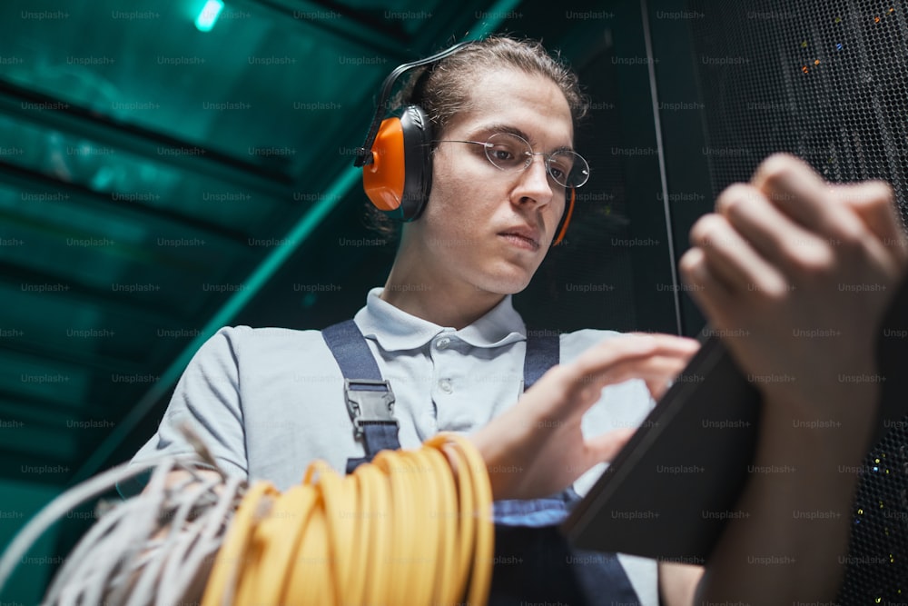 Low angle portrait of young network engineer using digital tablet in server room during maintenance work in data center, copy space