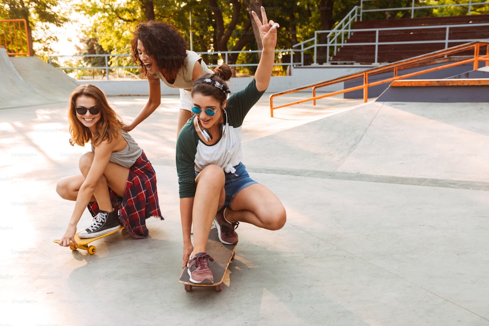 Drei fröhliche junge Mädchen mit Skateboards, die zusammen Spaß im Park haben