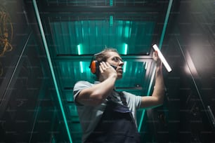 Low angle portrait of male network engineer speaking by smartphone in server room while working in data center, copy space