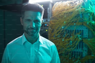 Portrait of handsome data engineer smiling at camera in server room while working with supercomputer in blue light, copy space