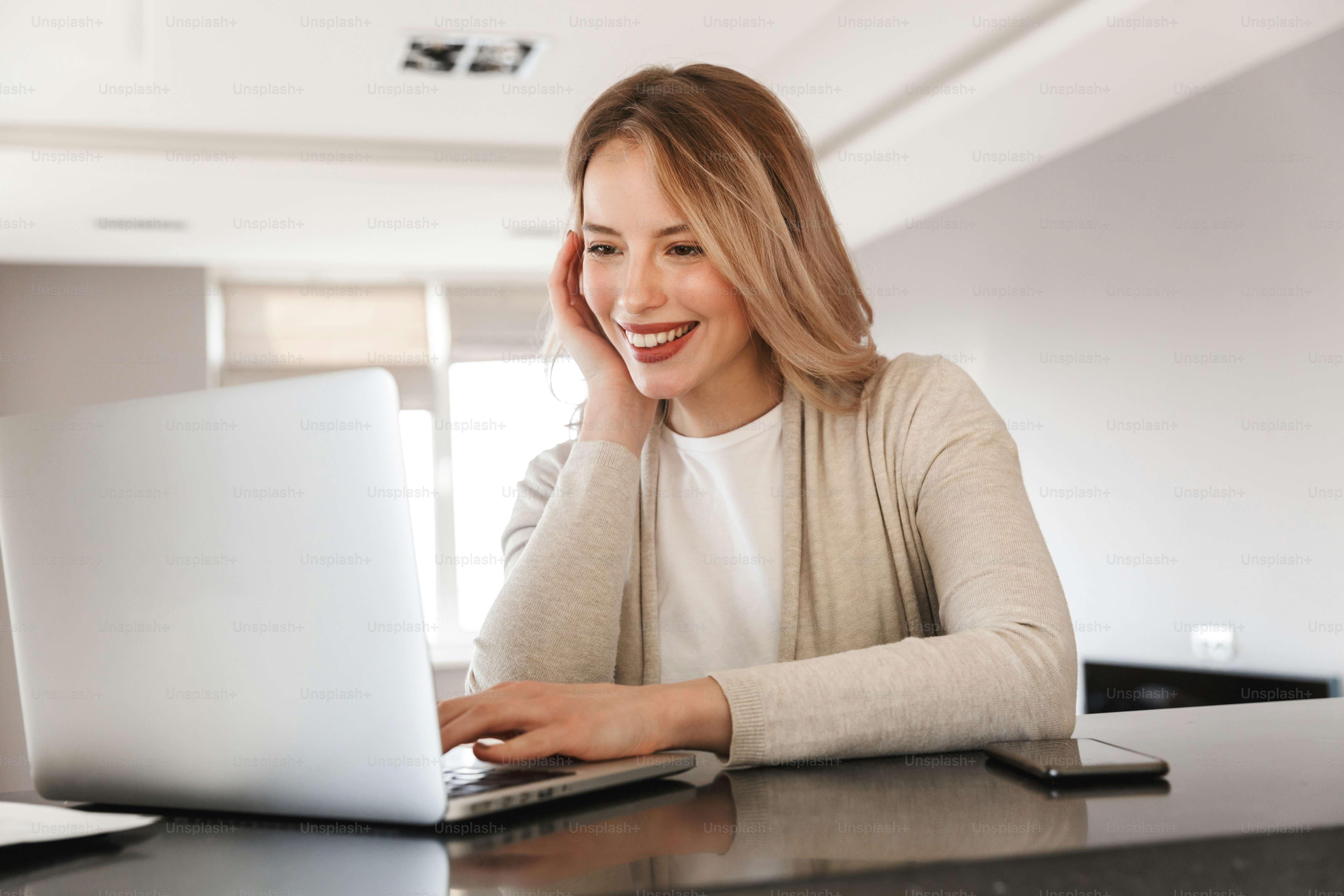 Image of a beautiful blonde woman posing sitting indoors at home using laptop computer.