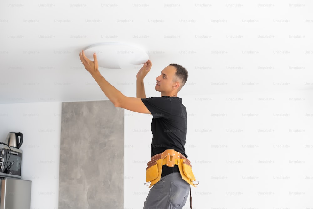 Worker installing lamp on stretch ceiling indoors. Space for text.
