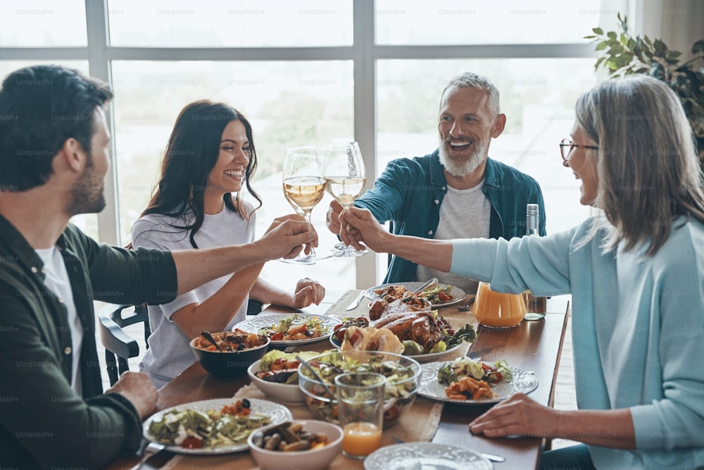Família feliz de várias gerações brindando uns aos outros e sorrindo enquanto jantam juntos