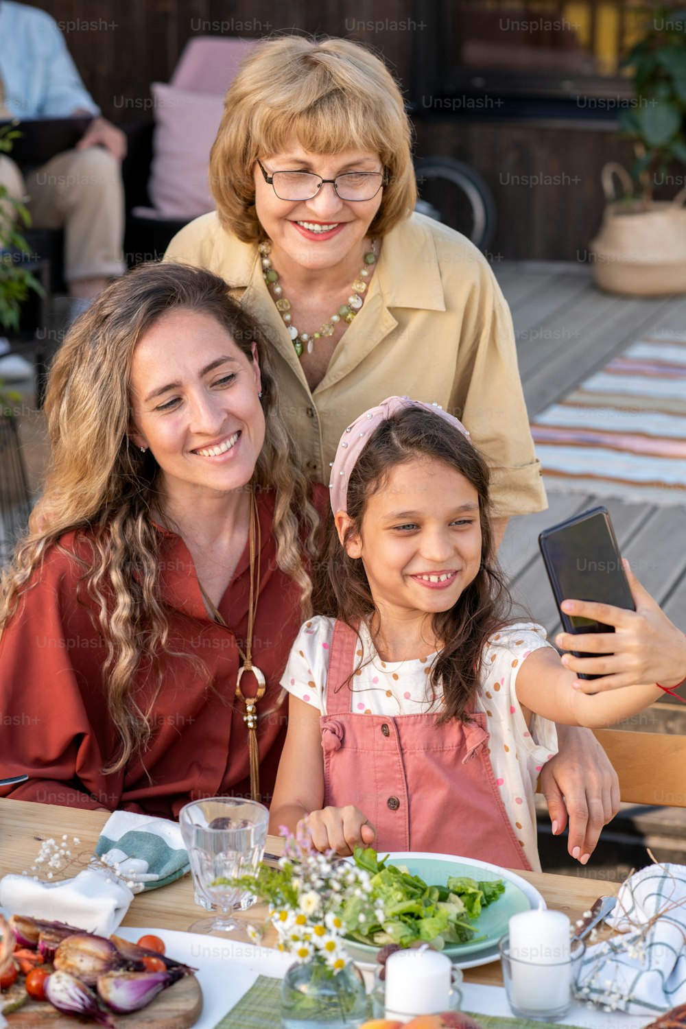Cute little girl taking selfie with her mother and grandmother at family celebration