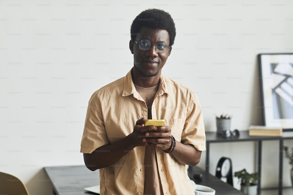 아프리카 청년의 초상화는 사무실에 서서 카메라를 보고 휴대전화를 사용한다