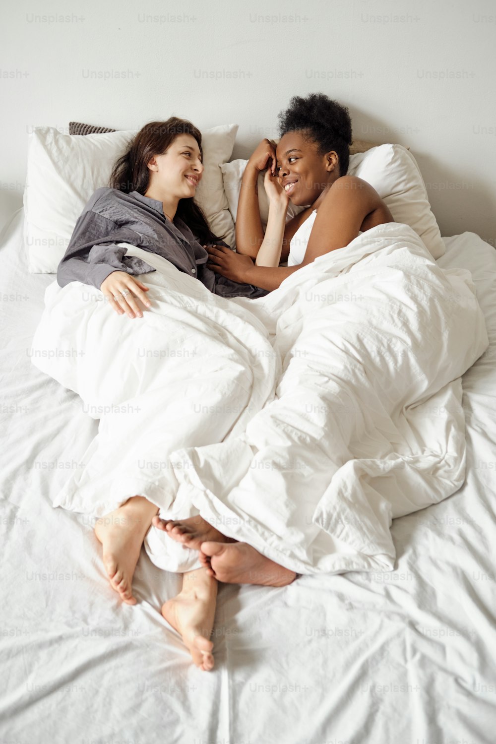 Lesbian couple lying in bed under white blankets and chatting in the morning