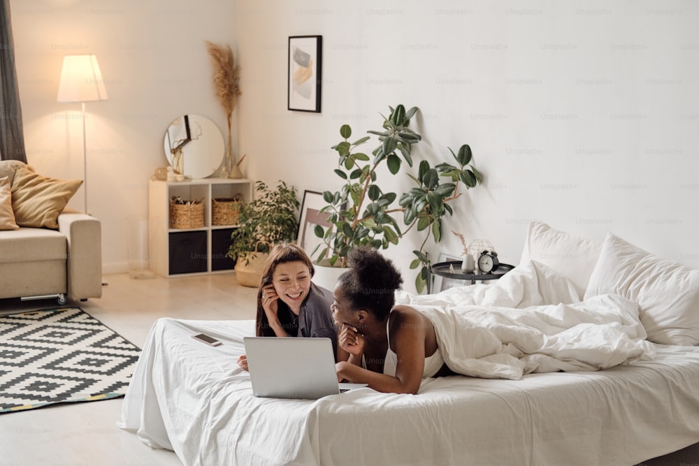 Dos chicas relajándose frente a la computadora portátil en la cama por la noche
