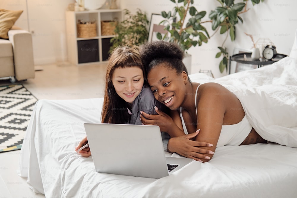 Alegre pareja de lesbianas mirando la pantalla de la computadora portátil durante la comunicación en línea