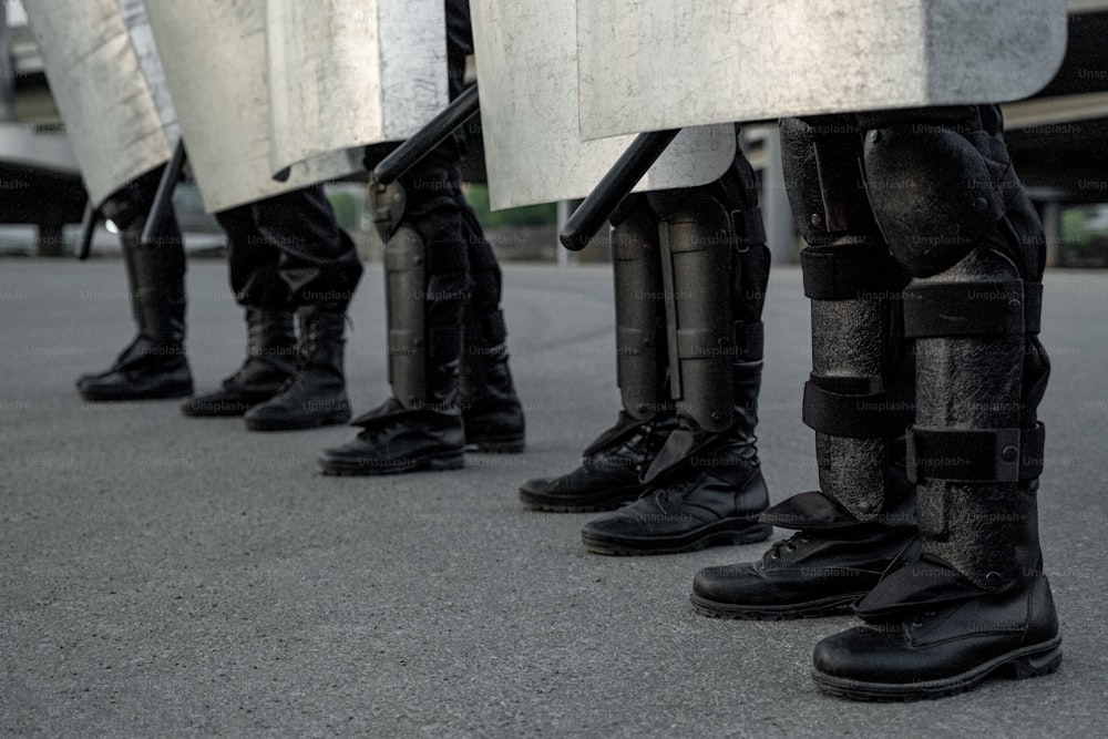 Group of riot police staff in black boots standing on asphalt at street and holding shields