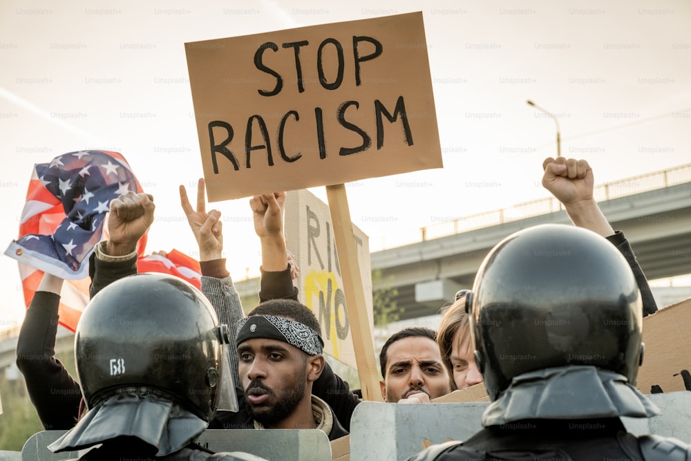 Group of displeased young American people raising fists and banner while asking to stop racism, police keeping crowd