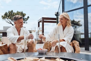 Beautiful mature couple in bathrobes enjoying fruits and champagne while relaxing in luxury hotel outdoors