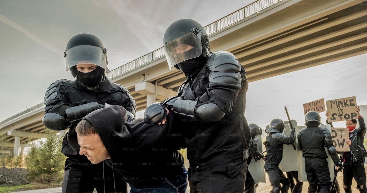 Riot police in body armors twisting man into uncomfortable position ...