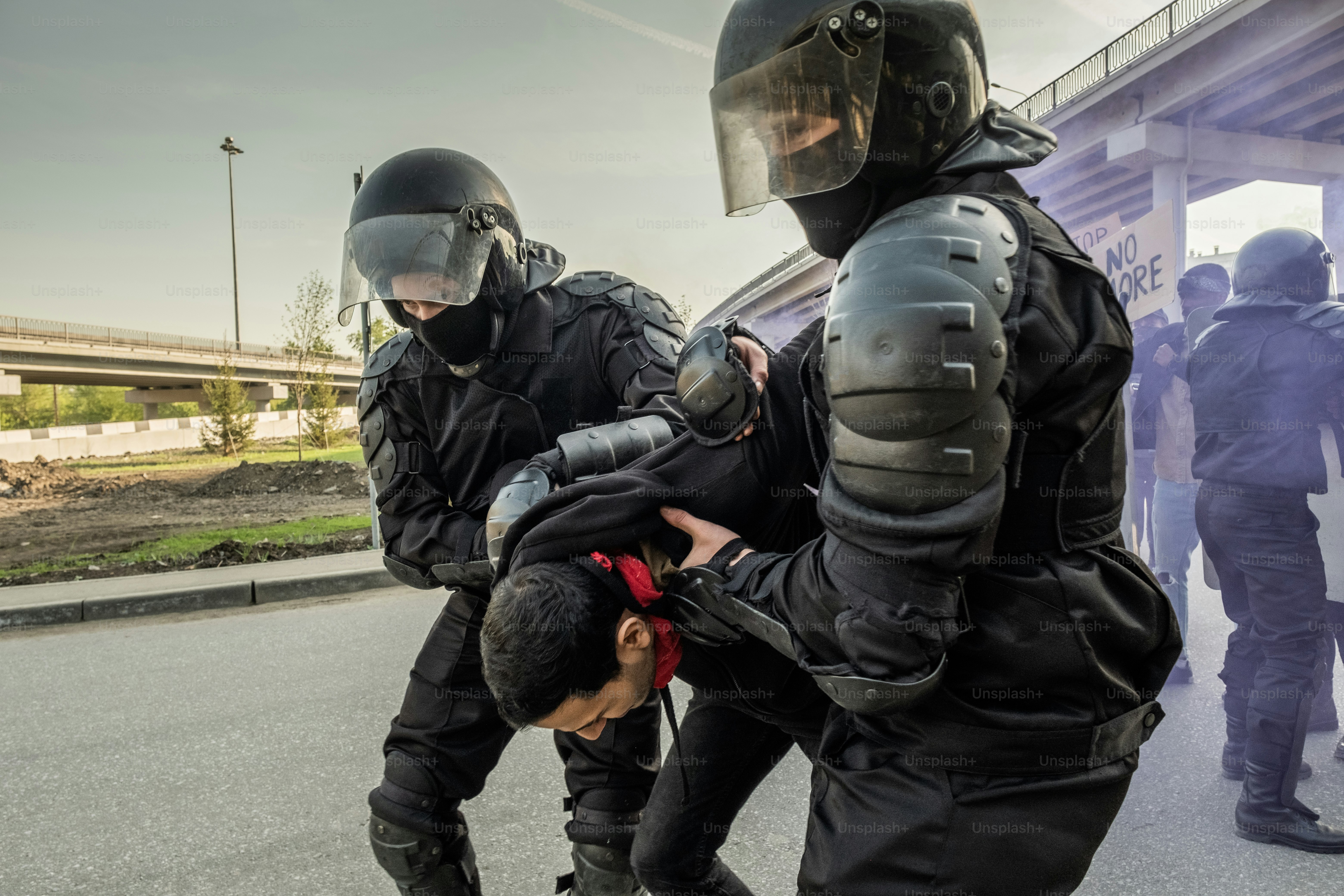 Skilled riot police in helmets holding hands of rebel behind his back while arresting people at rally