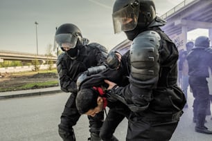 Skilled riot police in helmets holding hands of rebel behind his back while arresting people at rally