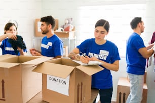 Weibliche Betreuerin kreuzt die Spendenkästchen an. Gruppe junger Freiwilliger hilft bei der Organisation von gespendeter Kleidung