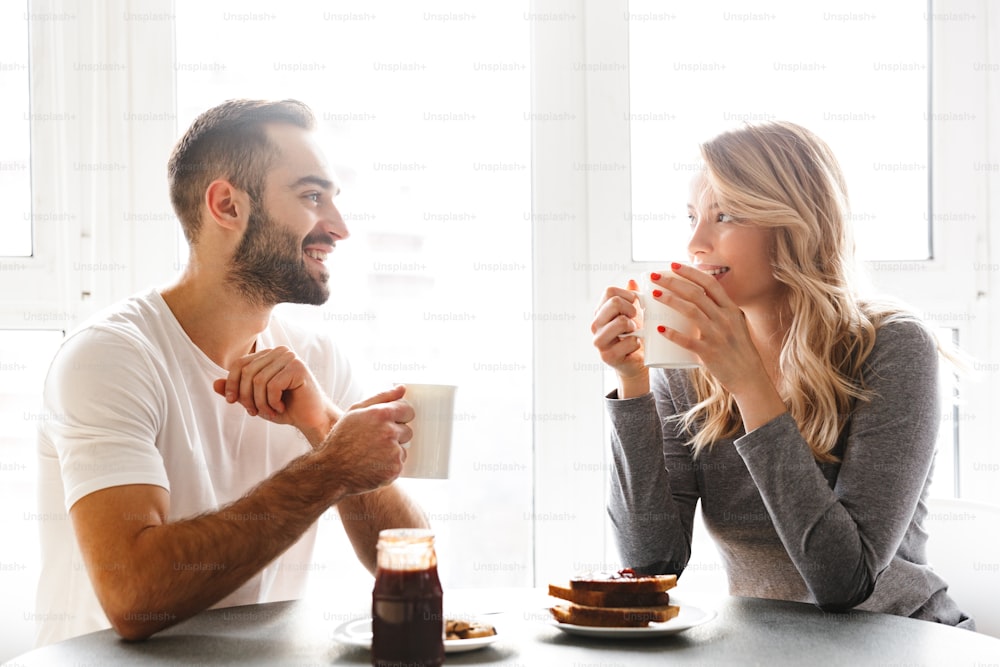 Image of amazing young loving couple sitting at the kitchen have a breakfast talking with each other.