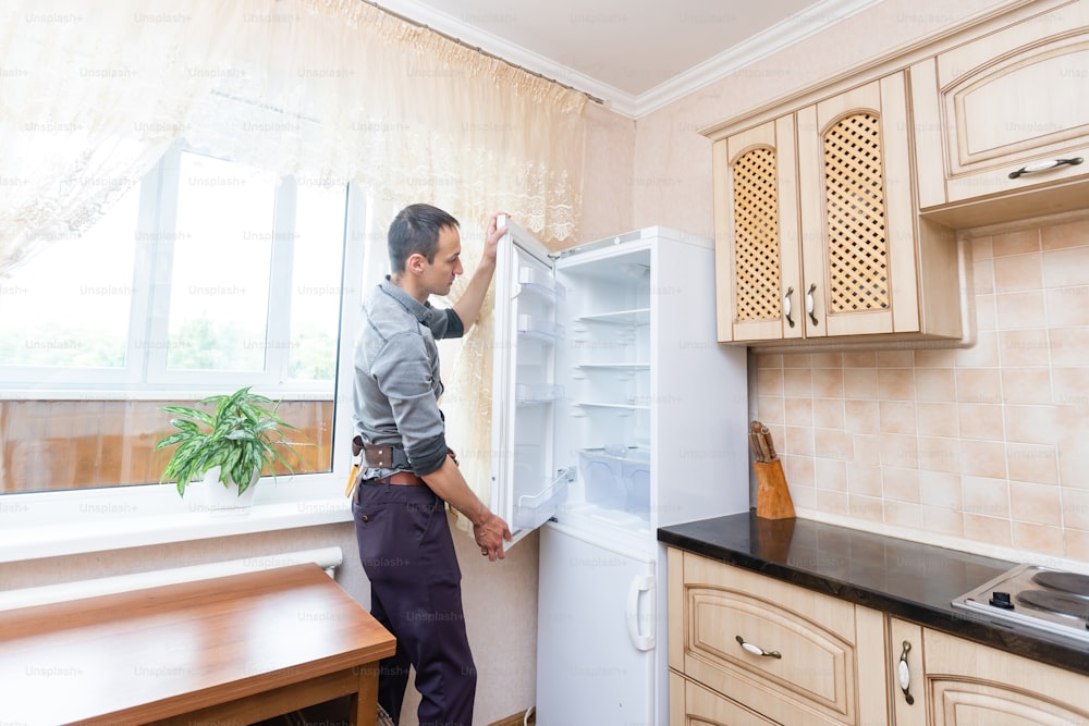 Jovem reparador masculino fixando geladeira na cozinha.