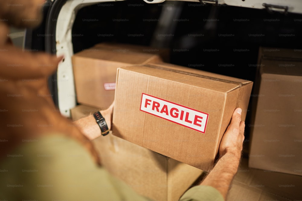 Close up of male delivery worker loading boxes into van at shipping service, copy space