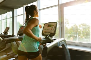 Side view of Young concentrated sports woman running on treadmill near the window in gym
