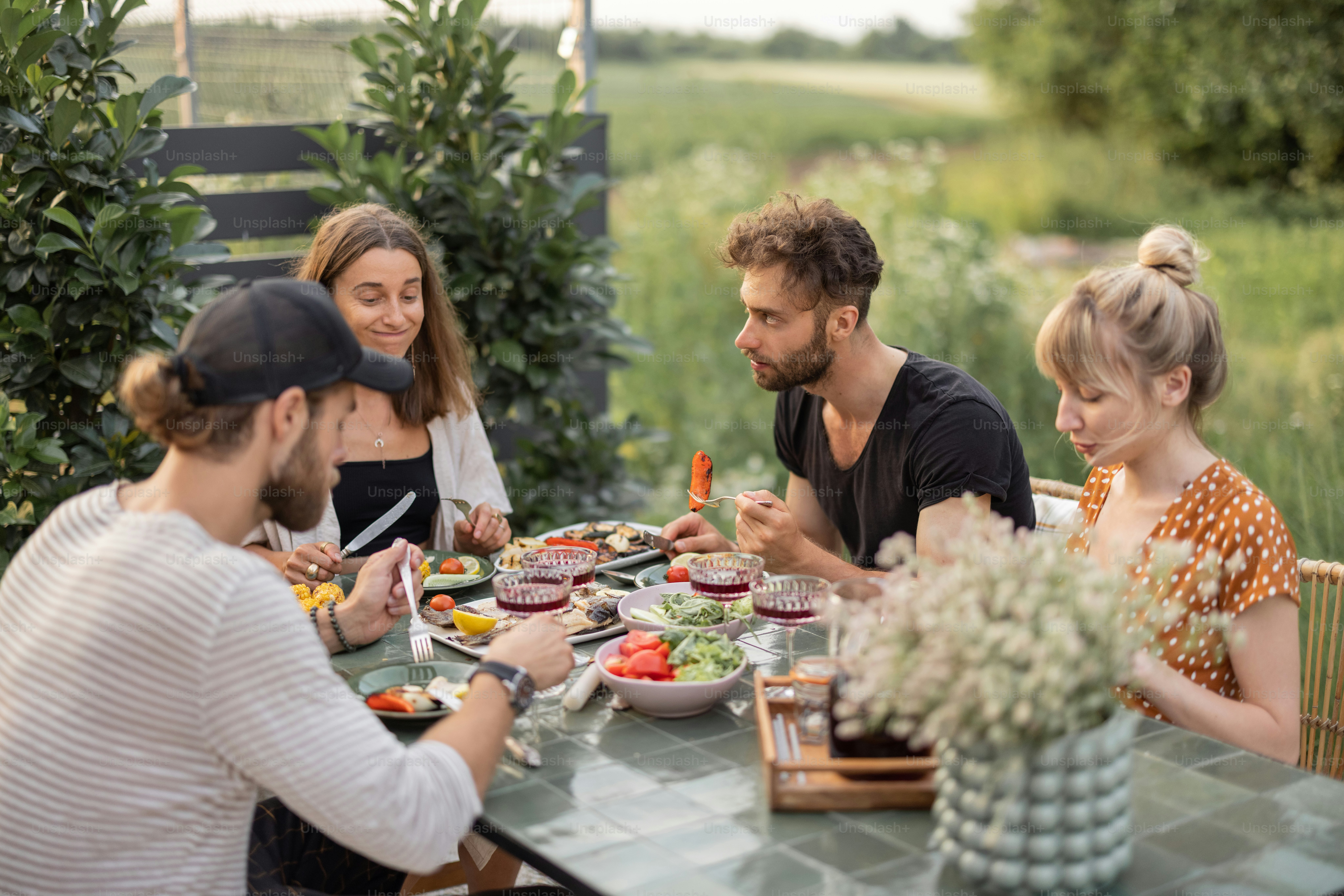 Petit groupe de jeunes amis déjeunent à l’extérieur, mangent des légumes et du poisson grillés et s’amusent dans la cour arrière
