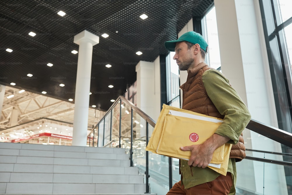 Side view portrait of delivery man holding parcels while walking up stairs to office building, copy space