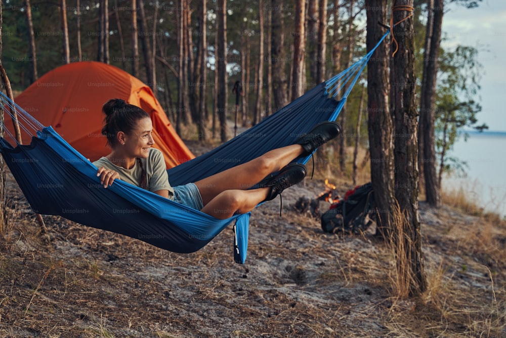 Female hiker placing her legs on hammock and half-rising to see the view of lake