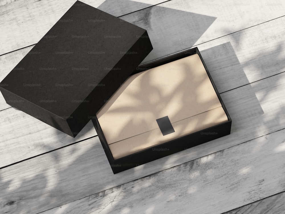 Maquete de Caixa de Presente texturizada preta aberta com papel de embrulho kraft e adesivo na mesa de madeira branca ao ar livre. Renderização 3D