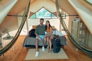 Junges liebevolles Paar, das auf Reisen auf einem Doppelbett im Glamping-Haus sitzt