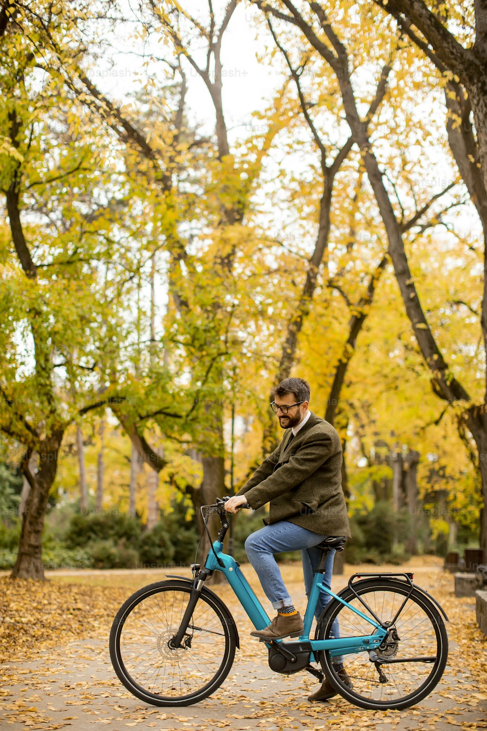 Jovem bonito com bicicleta elétrica no parque de outono