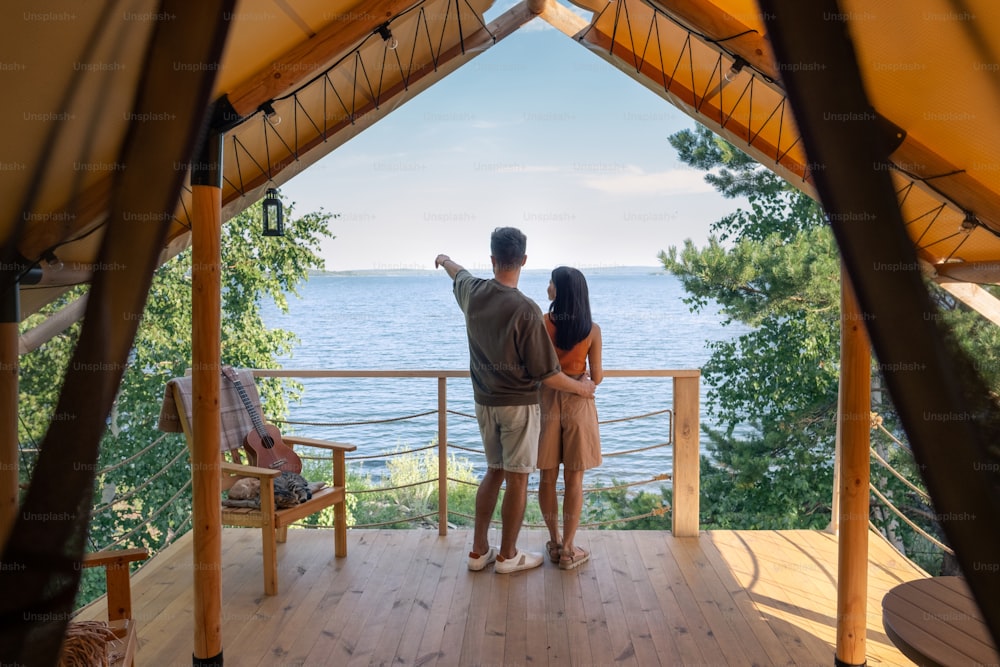 Backs of young man and woman standing in front of seaside during summer vacation