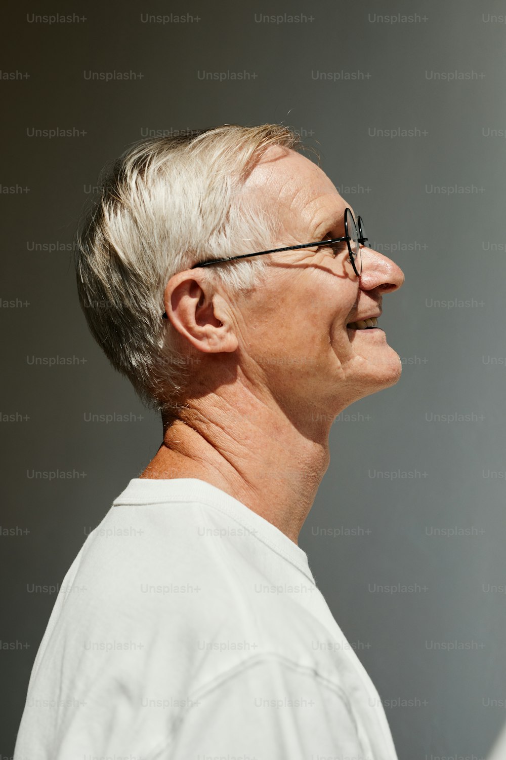 Minimal side view portrait of smiling senior man lit by sunlight against grey wall