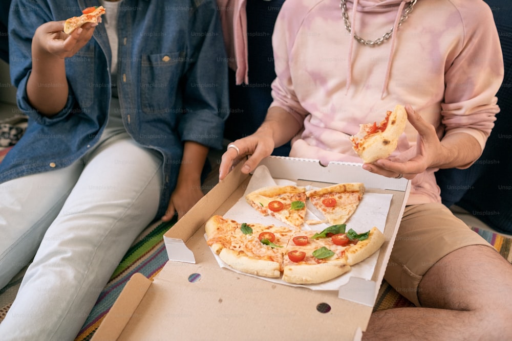 Deux adolescents détendus en tenue décontractée mangeant de la pizza dans une boîte tout en étant assis par terre