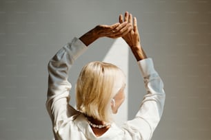 Back view portrait of elegant mature woman dancing lit by sunlight against white wall, copy space