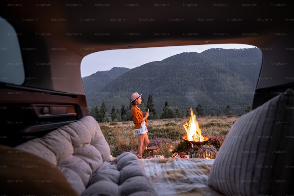 Frau genießt Lagerfeuer beim Picknick in den Bergen, Innenansicht von einem Kofferraum. Camping und Urlaub in den Bergen alleine, Anreise mit dem Auto Konzept