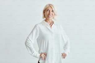 Waist up portrait of elegant mature woman smiling at camera while posing confident against white background, copy space