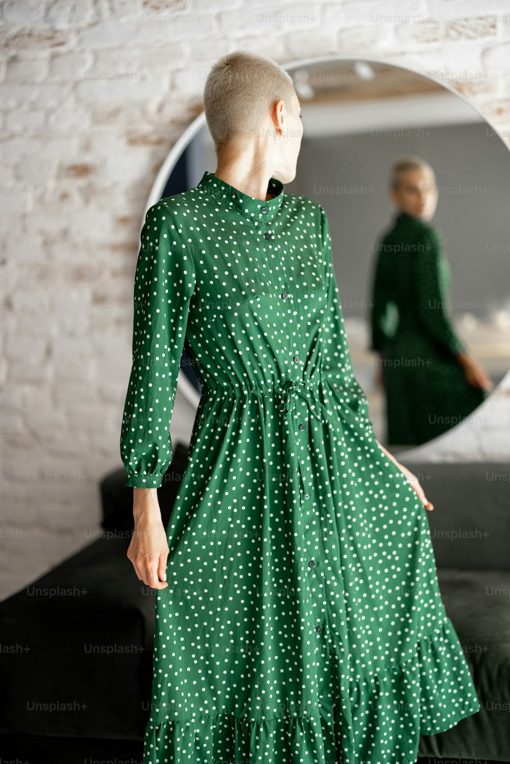 Stylish woman in green dress looks at herselfes in the mirror, getting ready to go out. Female style and beauty concept