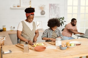 Young African woman and her son cooking breakfast or lunch by kitchen table