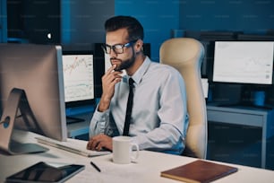 Konzentrierter junger Mann, der am Computer arbeitet, während er lange im Büro bleibt