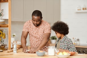 Mignon petit garçon regardant son père mettre de la pâte sous forme de cuisson tout en cuisinant des pâtisseries maison