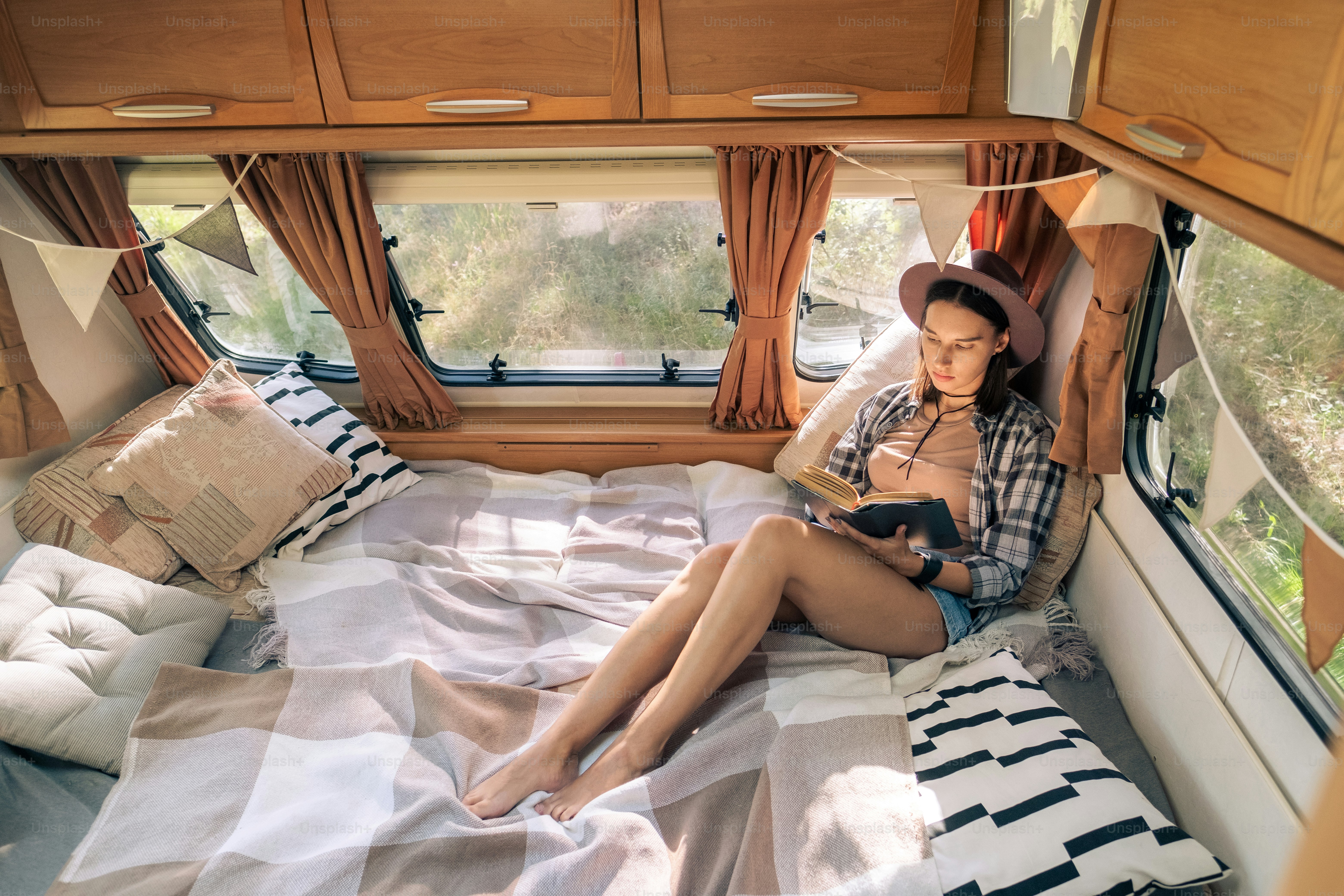 Young restful woman reading book on alrge comfortable bed inside travel house