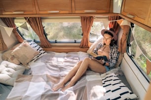 Young restful woman reading book on alrge comfortable bed inside travel house