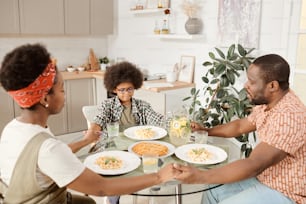 Young African family of three praying before dinner by served table with their eyes closed