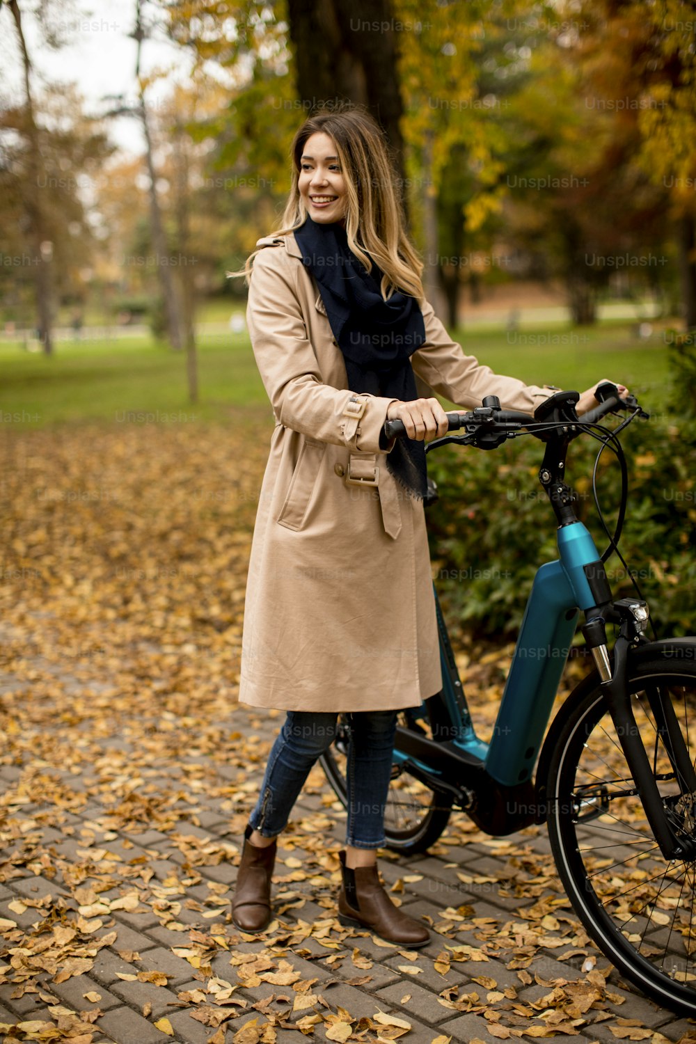 Mujer joven y bonita con bicicleta eléctrica en el parque de otoño