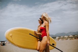 Deux jolies jeunes femmes avec paddle board sur la plage un jour d’été