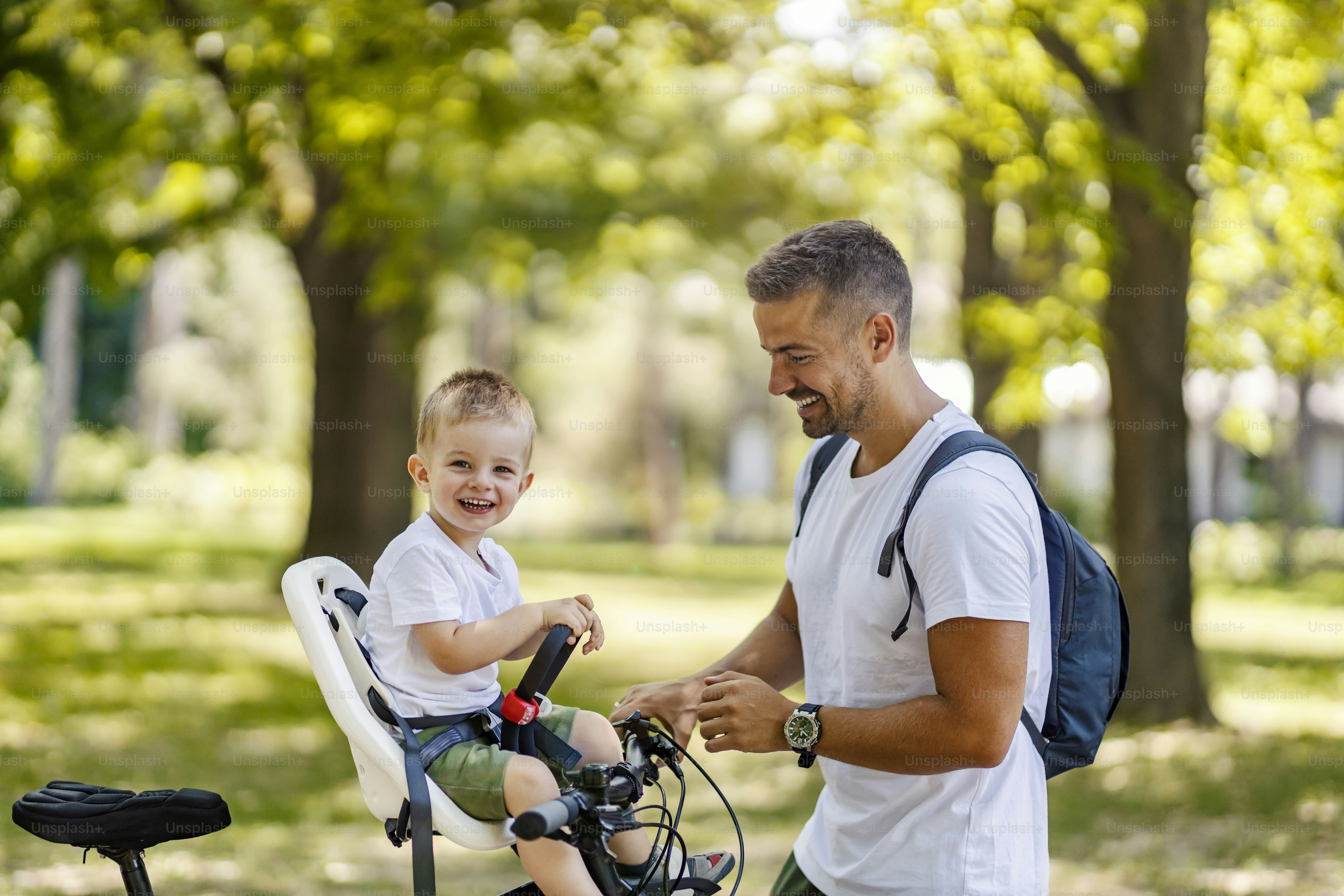 Getting ready for the bike ride. Father and son bonding time in nature. A cute boy is sitting in a bicycle basket while his father prepping his basket bells for the bonding time. Smiling together