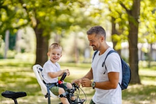 Getting ready for the bike ride. Father and son bonding time in nature. A cute boy is sitting in a bicycle basket while his father prepping his basket bells for the bonding time. Smiling together