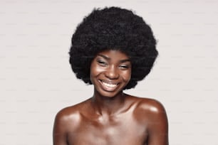 Portrait of beautiful young African woman looking at camera and smiling while standing against gray background