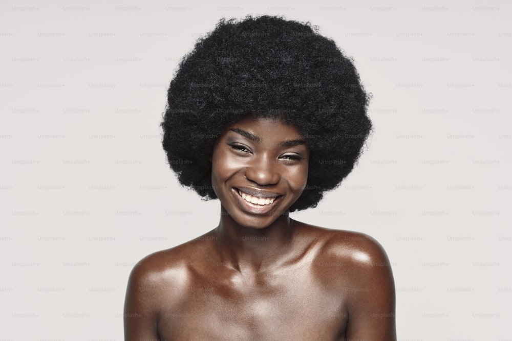 Portrait d’une belle jeune femme africaine regardant la caméra et souriant debout sur fond gris